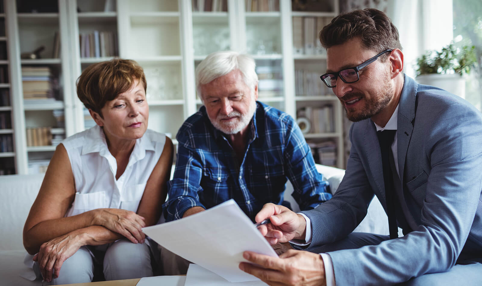 A man, a lawyer, looks over documents on a couch with a woman beside him, both focused on the conversation.